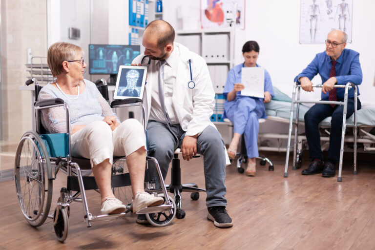 Physician explaining diagnosis to handicapped senior woman in wheelchair. Man with disabilities ,walking frame sitting in hospital bed. Health care system, clinic patients.